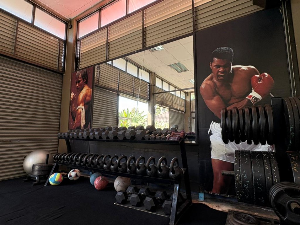 Dumbbell rack and kettlebells beside the Muhammad Ali mural at Bambu