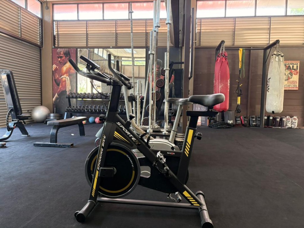 Spin bike with heavy bags and Muay Thai mural in the background at Bambu