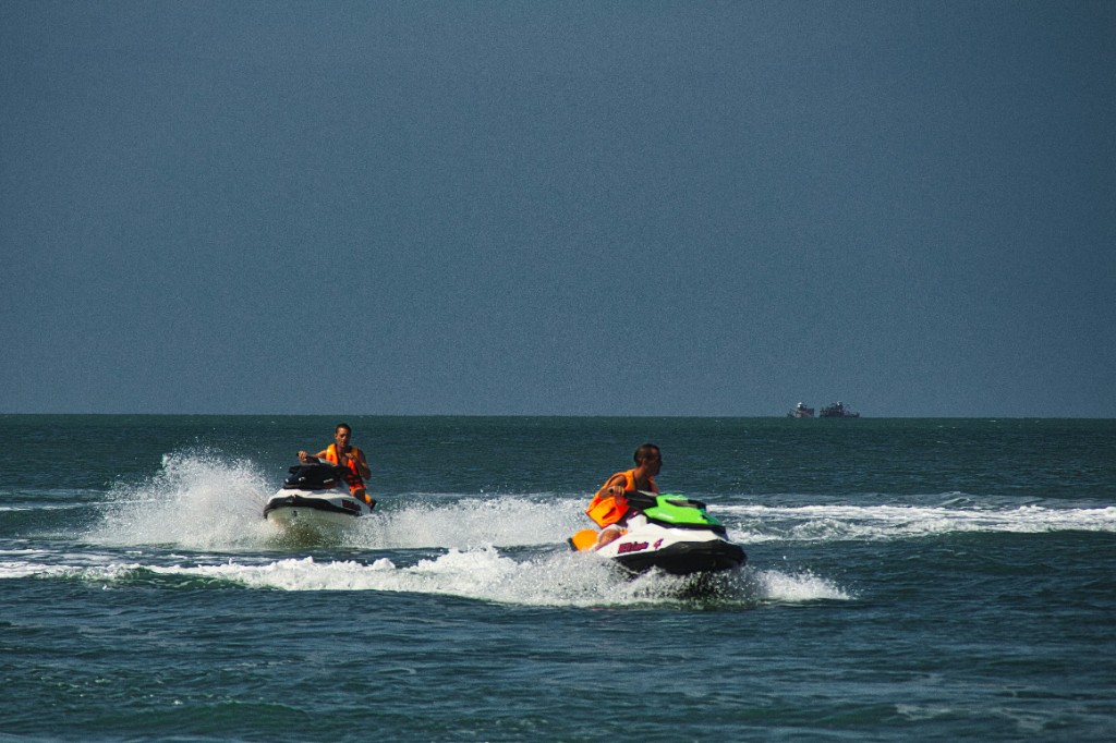 Two riders on jet skis crossing deep blue Langkawi waters with spray behind them